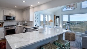 A modern kitchen with white cabinetry, a large island, and a view of the landscape through large windows.