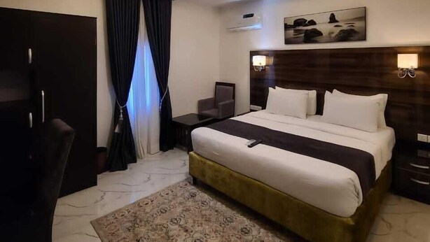 Quarto de hotel moderno com uma cama grande, uma mesa, uma cadeira e um lustre no teto.