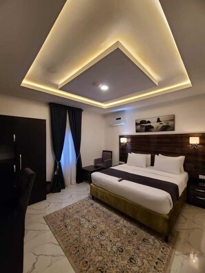 A modern hotel room with a large bed, a desk, a chair, and a ceiling light fixture. - Mapleviewhotels and Suite Limited (Lekki)
