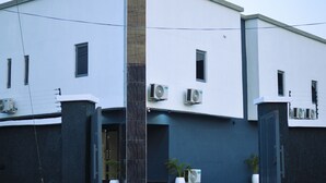 Um edifício moderno com várias unidades de ar condicionado, uma entrada central e plantas em vasos.