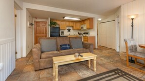 A living room with a sofa, a coffee table, and a chair. There is a kitchen area with wooden cabinets and a microwave. - Trails End Mountainside Condo: Ski-In/Out, Downtown Breck (Breckenridge)