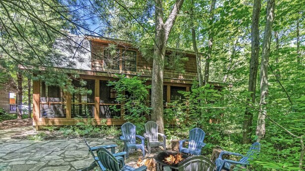 Een chalet met een stenen terras, buitenmeubels en een vuurkorf.
