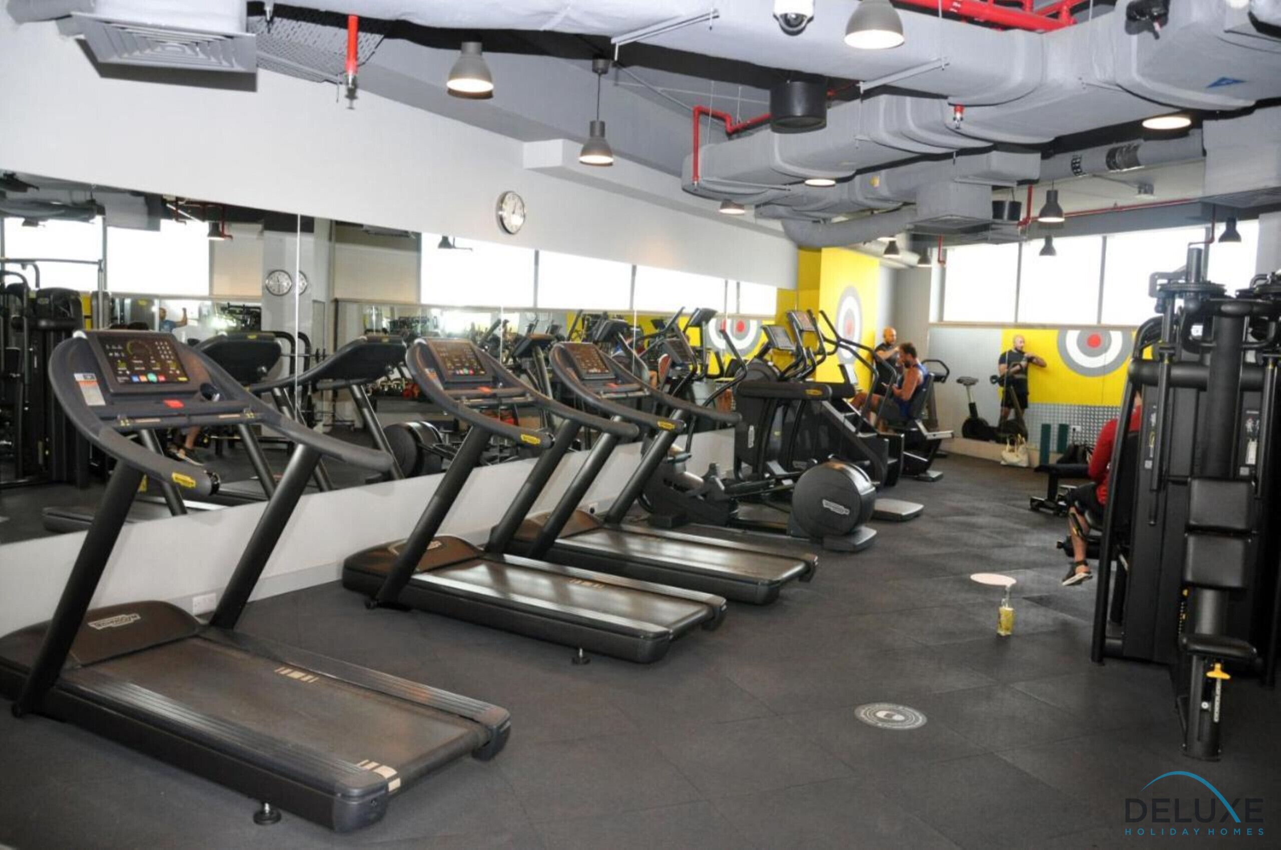A gym with multiple treadmills, weight machines, and a yellow wall with a target design.
