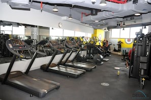 Uma academia com esteiras, aparelhos de musculação e uma parede amarela com desenho de alvo.