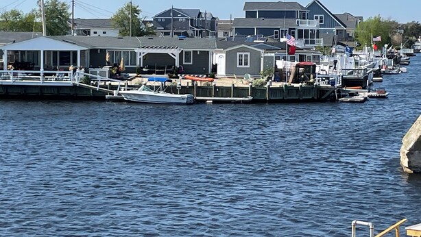 A marina with docked boats, a covered boat house, and residential buildings in the background. - Mystic Island Bay Breeze, Beautiful waterfront sunsets waiting (Little Egg Harbor Township)
