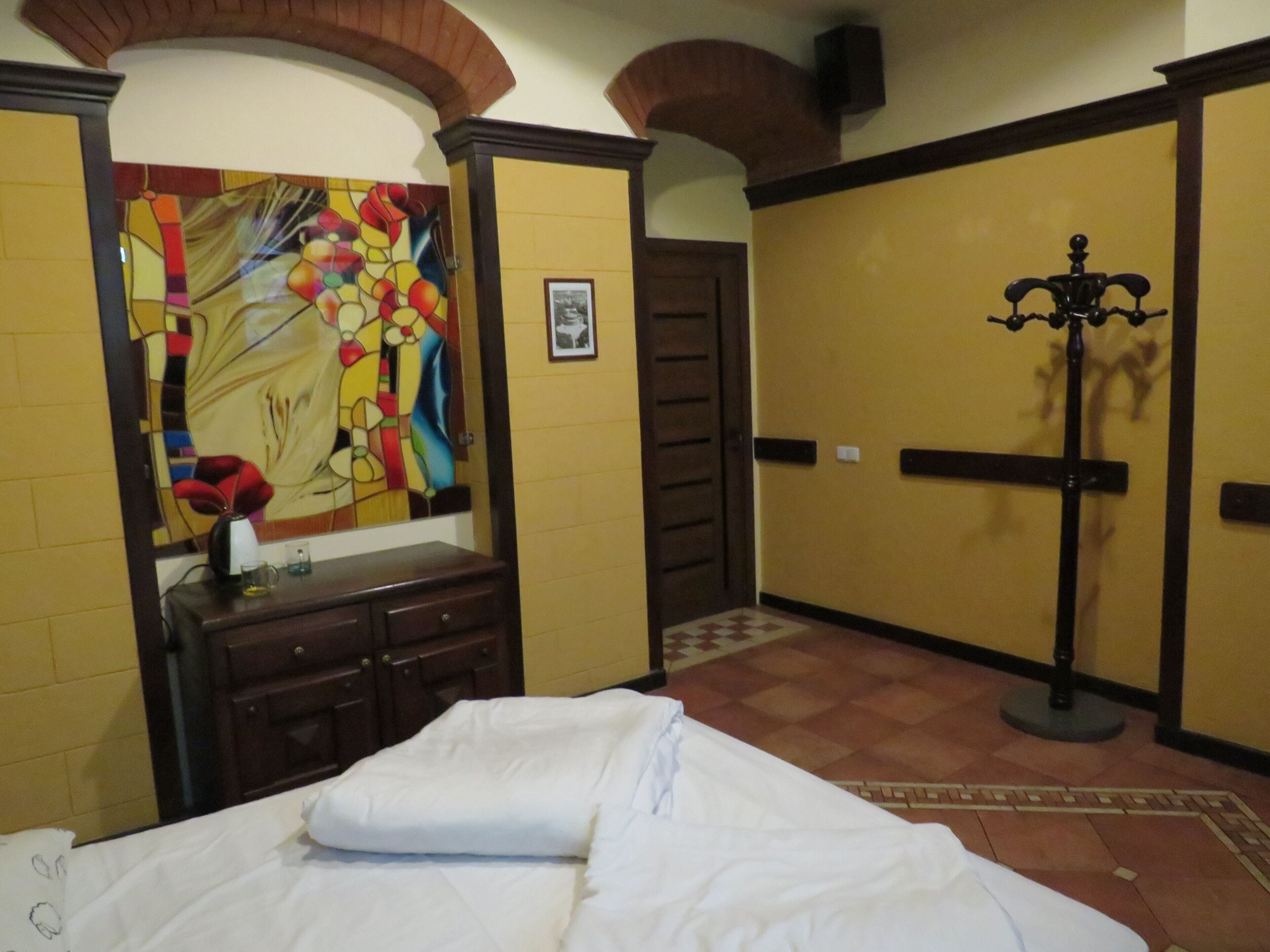 A hotel room with a bed, a dresser, a mirror, and a colorful abstract painting on the wall.