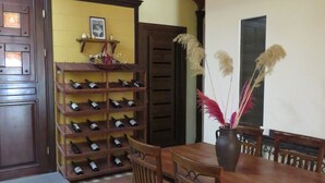 A dining area with a wooden table and chairs, a wine rack with bottles, and a vase with dried flowers.