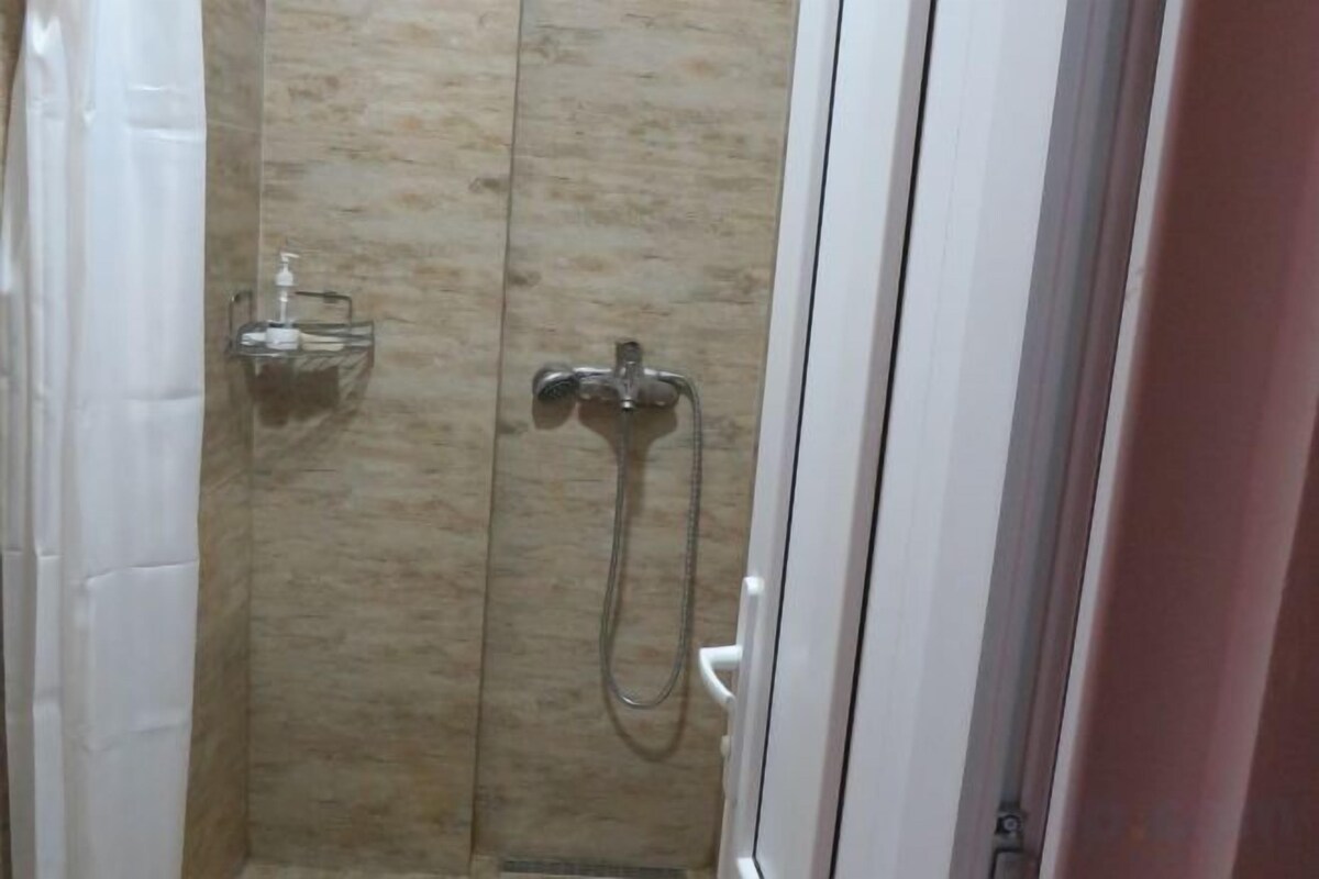 A shower area with a glass enclosure, a handheld showerhead, and a wall-mounted faucet.