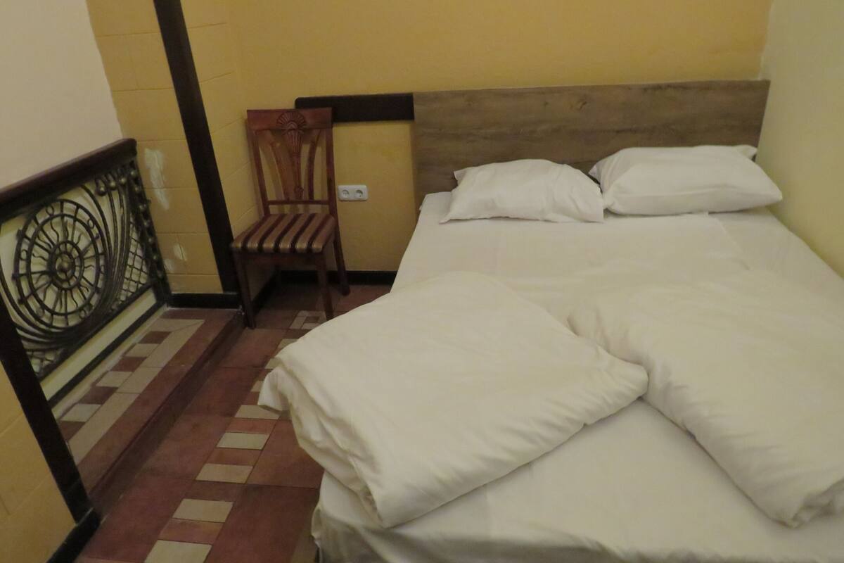 Una cama bien hecha con sábanas blancas en una habitación con paredes amarillas y cabecera de madera.