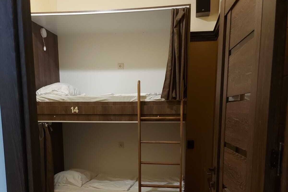 Una habitación pequeña y estrecha con dos literas, numeradas 13 y 14, suelo de madera y una puerta a la derecha.