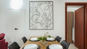 Ein Esszimmer mit Holztisch, gedeckt für vier Personen, einem modernen abstrakten Kunstwerk darüber und einem roten Stuhl links.