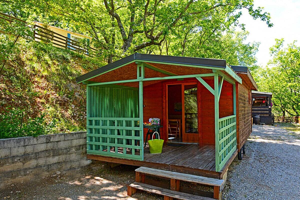 Una cabaña de madera con un porche, una mesa con una cesta y un banco.