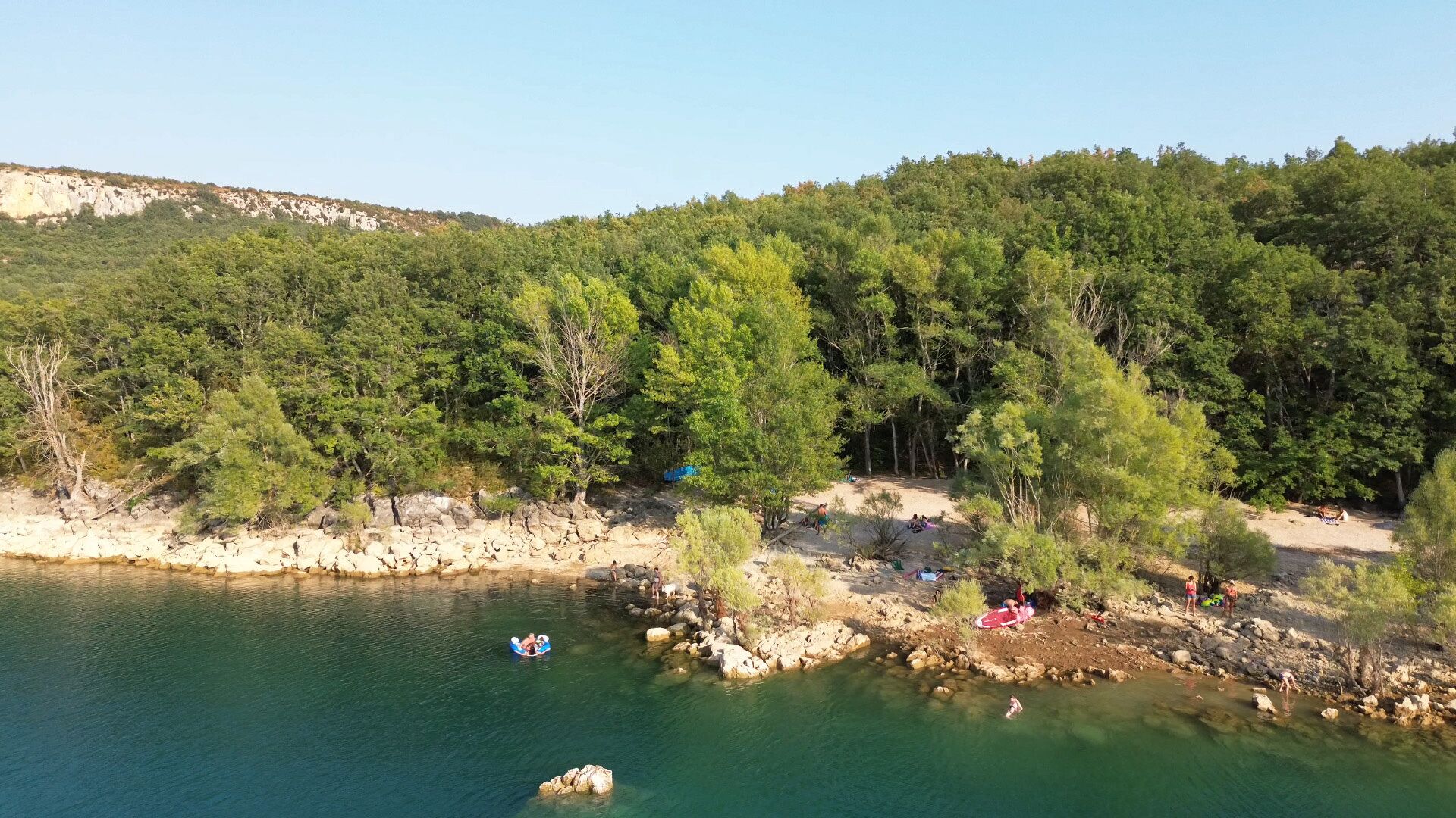 Un paysage naturel caractérisé par un plan d’eau limpide, une côte rocheuse et une forêt dense.