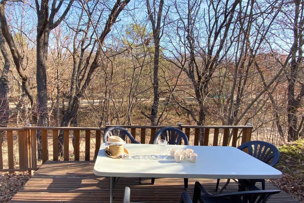 Una terraza de madera con una mesa y sillas, rodeada de árboles.