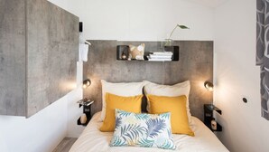 Ein modernes Schlafzimmer mit Beton-Kopfstütze, zwei Nachttischen mit Lampen, einem Bett mit gelb-gemusterten Kissen und einer kleinen Ablagefläche mit Dekoration.
