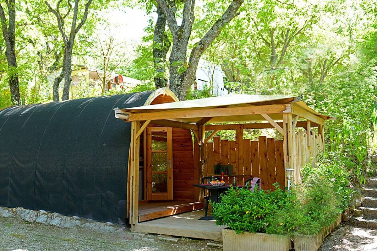 Un espacio al aire libre techado con estructura de madera, una mesa con sillas y un pequeño jardín.