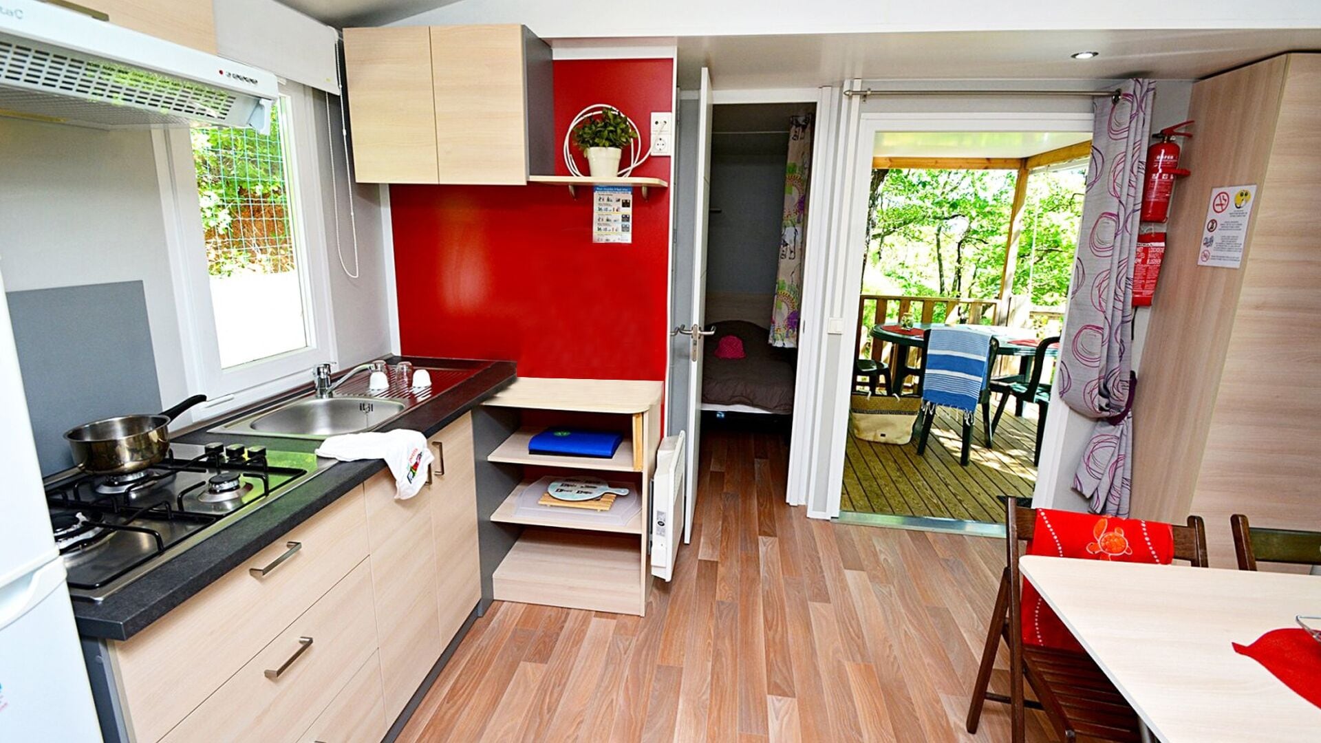 A compact kitchen with a gas stove, sink, and wooden cabinets. A small dining area with a table and chairs is visible through an open door.