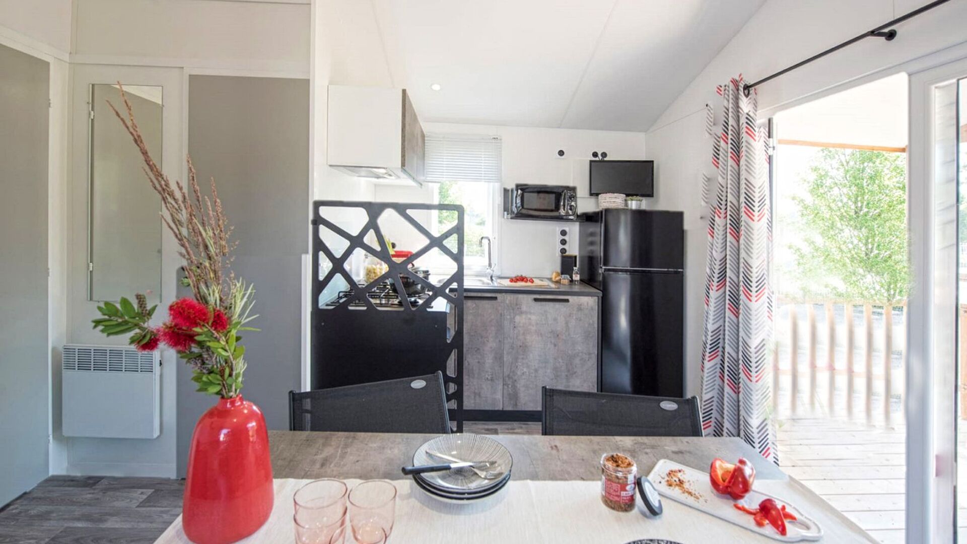 A compact kitchen with a gas stove, microwave, and black refrigerator. A dining table with a vase of flowers and a few plates is visible.