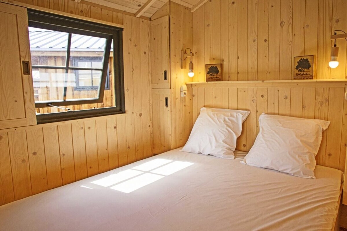 A wooden cabin room with a bed, a window, and wall-mounted lights.