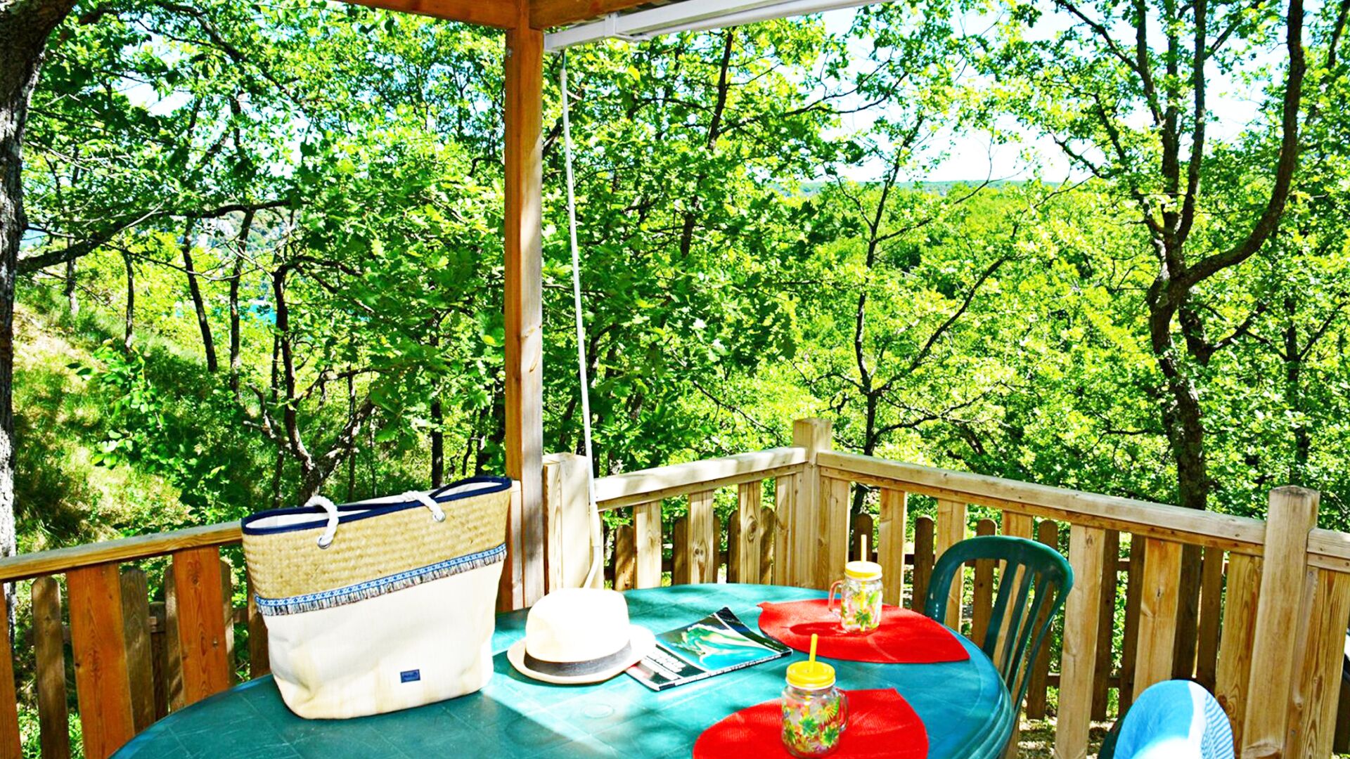 A wooden deck with a table set for two, surrounded by lush greenery.