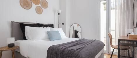 A modern bedroom with a bed, bedside table, lamp, and a view of the outdoors.