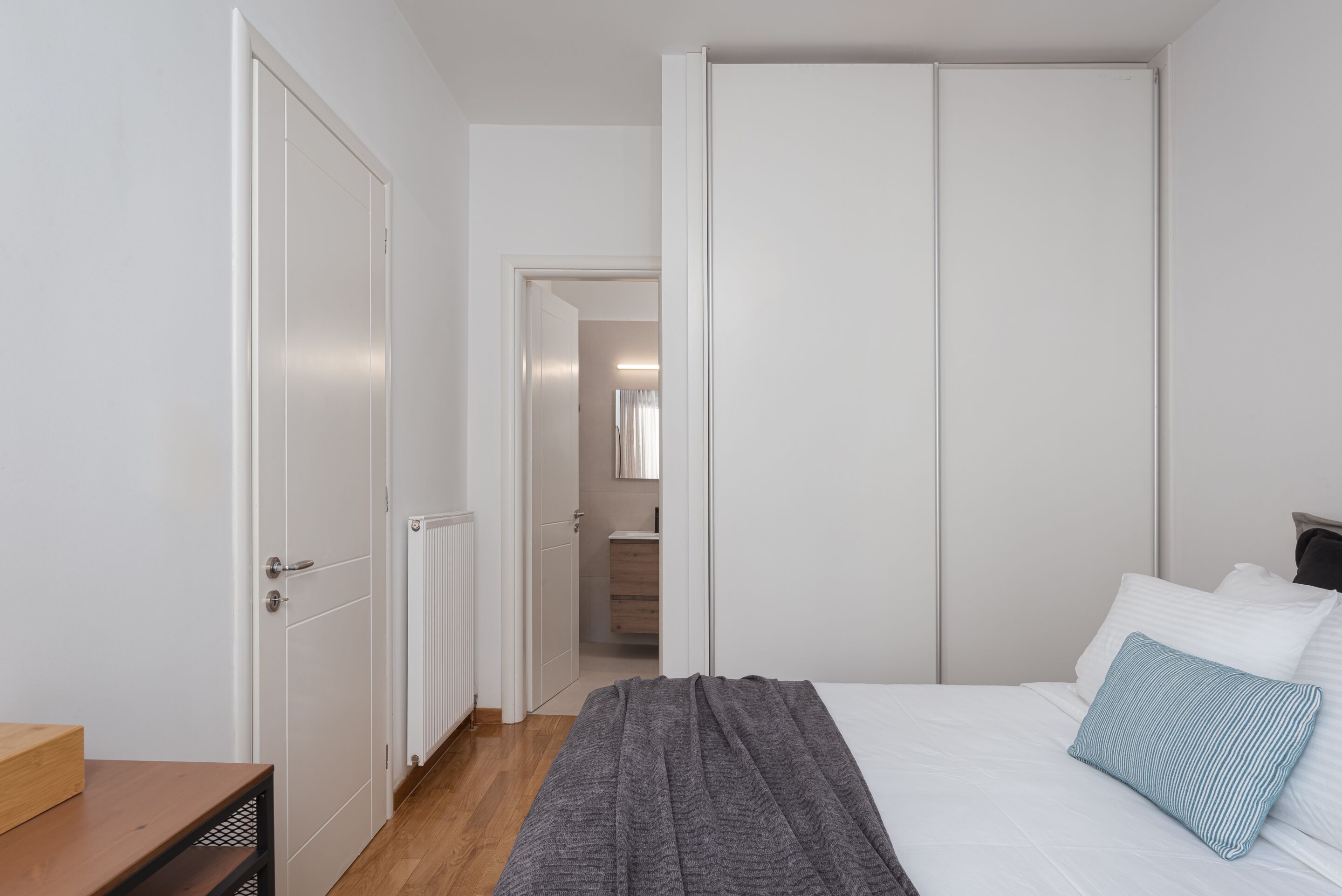 Une chambre à coucher avec un lit, une table de chevet en bois, une couverture grise et un oreiller blanc.