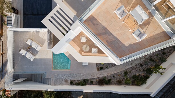 Una vista aerea di un hotel moderno con piscina sul tetto, area salotto all'aperto e un giardino curato.