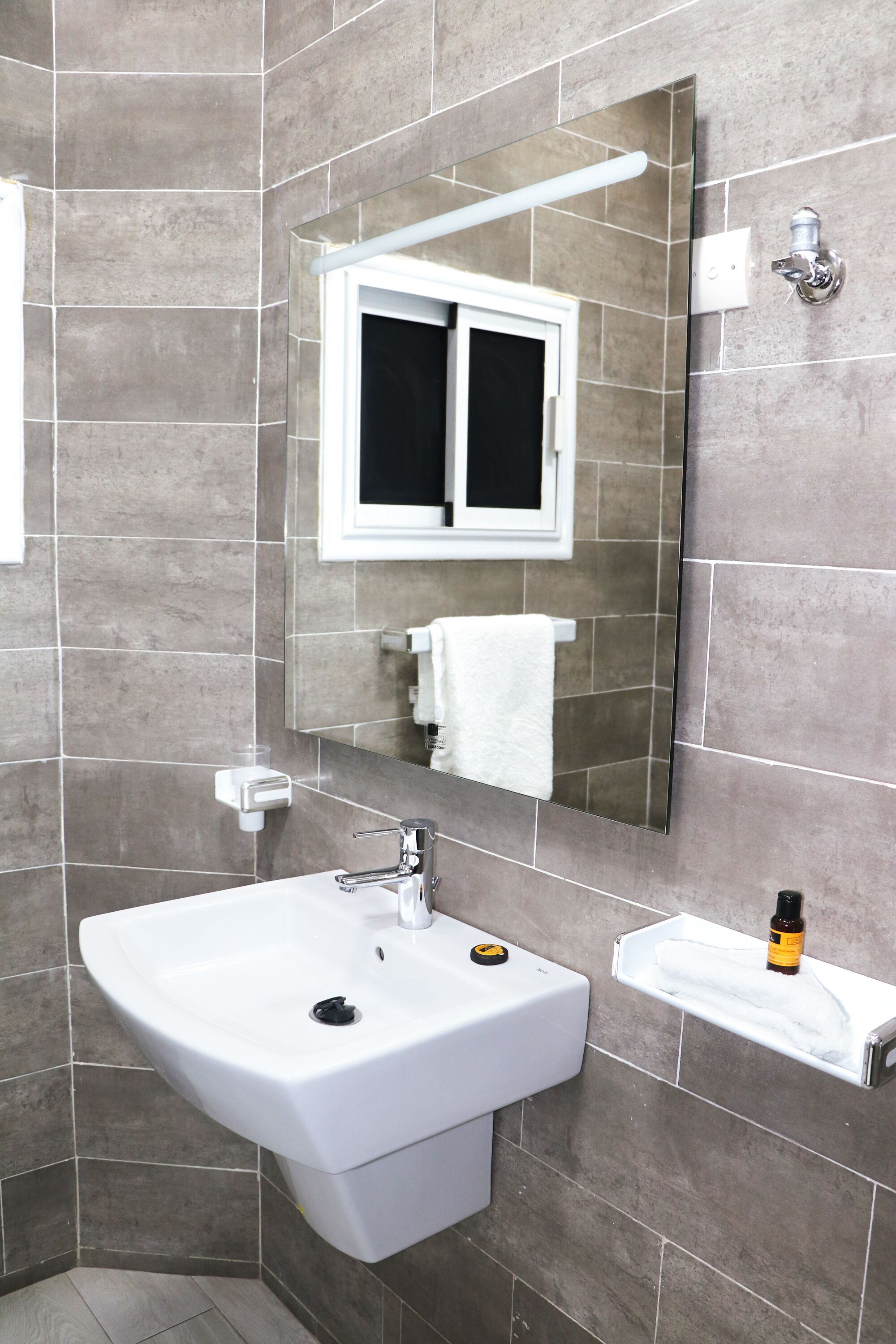 A bathroom with a white sink, a mirror, and a window above the mirror.