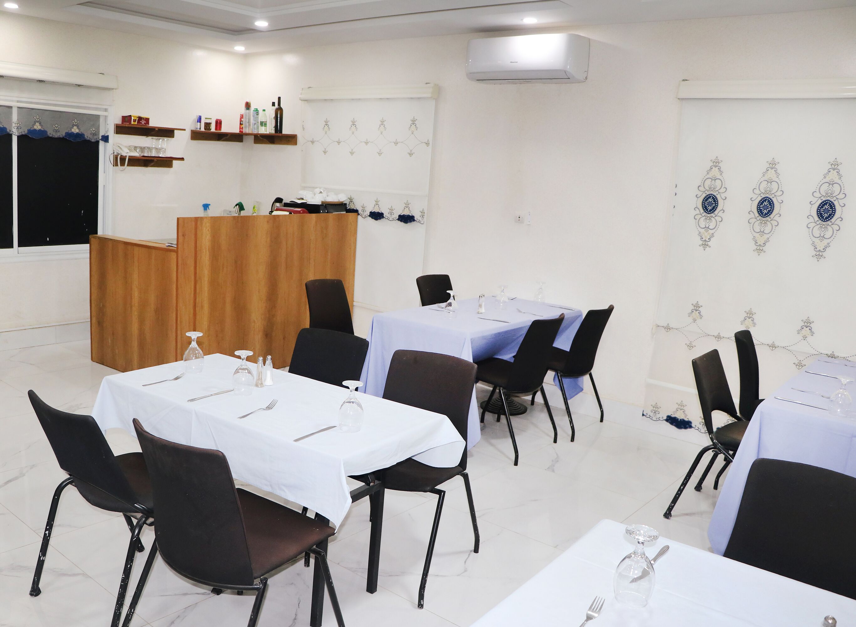 Un comedor con mesas dispuestas para cuatro, sillas negras, un atril de madera y diseños decorativos en las paredes.
