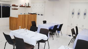 Un comedor con mesas dispuestas para cuatro, sillas negras, un atril de madera y diseños decorativos en las paredes.