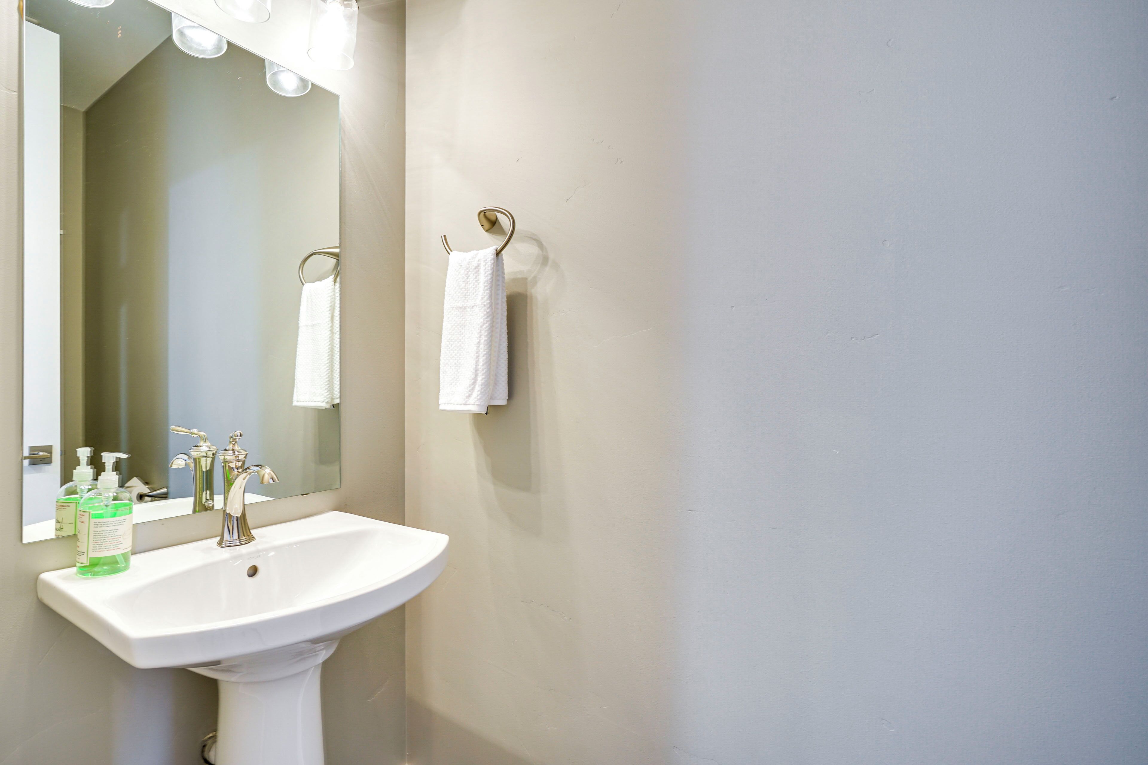 Une salle de bain avec un lavabo blanc, un miroir et deux serviettes blanches accrochées à des crochets.
