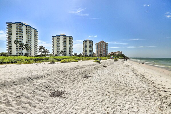 A beach with high-rise buildings, palm trees, and a clear sky.