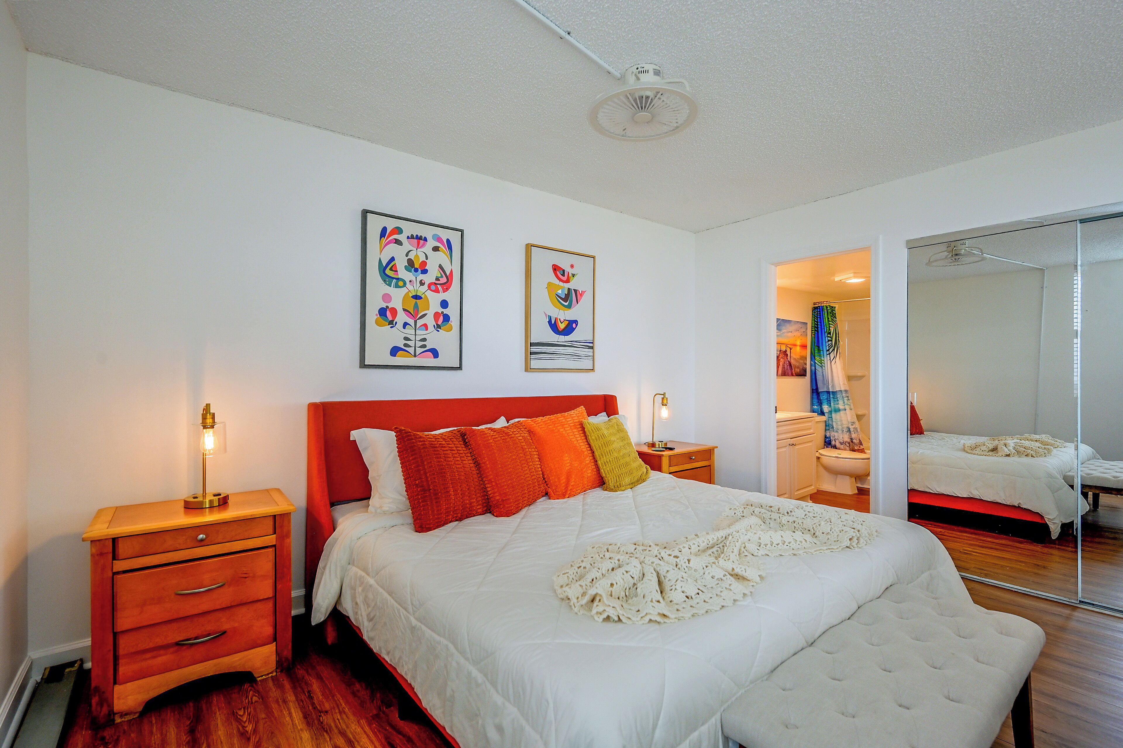 A bedroom with a bed, nightstands, a mirror, and artwork on the wall.