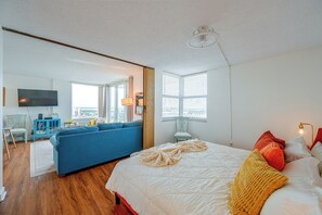 Een moderne slaapkamer met een groot bed, een blauwe bank en uitzicht op de stad door het raam.