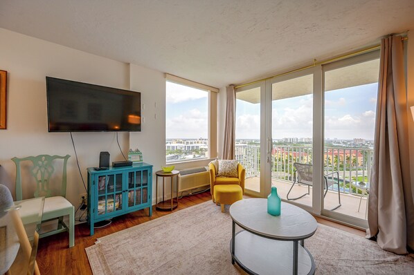 A living room with a flat-screen TV, a blue cabinet, a yellow armchair, and a round table. - Fort Myers Beach Studio w/ Balcony & Views! (Fort Myers Beach)