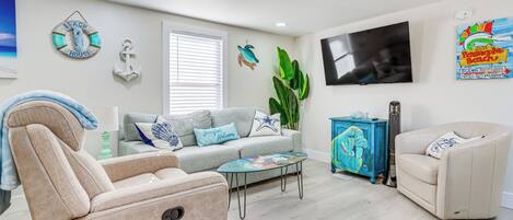 Un salon avec un canapé beige, un fauteuil bleu, une table basse et un téléviseur fixé au mur.