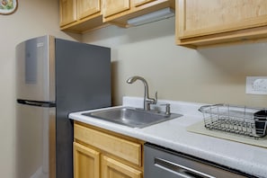 A kitchen with wooden cabinets, a stainless steel refrigerator, a sink with a faucet, and a dish rack. - Englewood Condo w/ Pool Access: 1 Mi to Light Rail (Englewood)