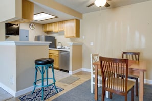 A compact kitchen with wooden cabinets, a built-in microwave, and a dishwasher. There is a small island with a stool and a dining table with chairs. - Englewood Condo w/ Pool Access: 1 Mi to Light Rail (Englewood)