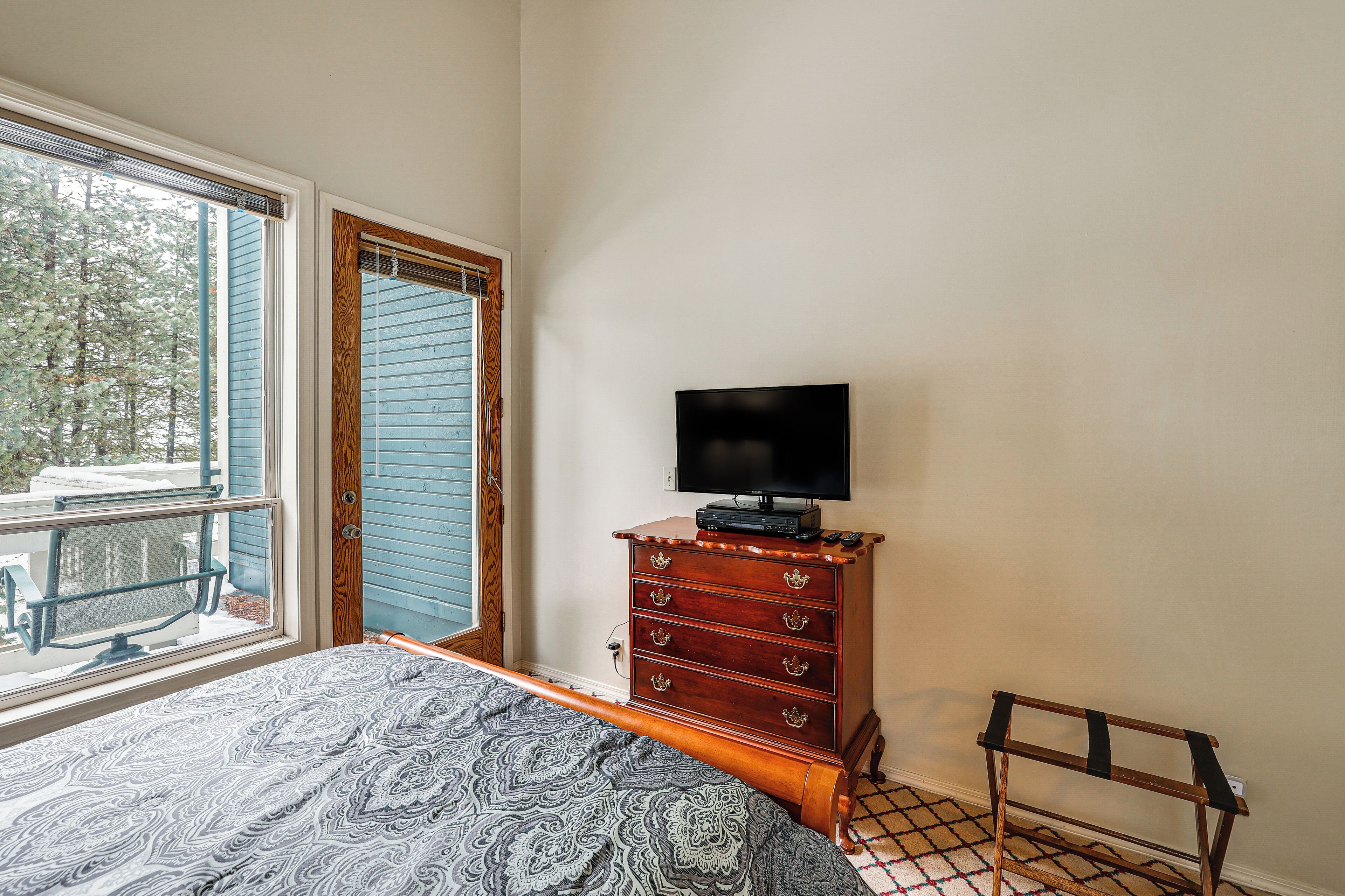 A bedroom with a bed, a dresser with a television, a window, and a door.