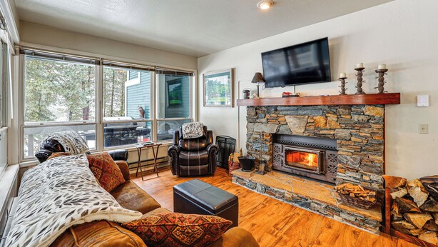 A cozy living room with a stone fireplace, comfortable seating, a large window, and a flat-screen TV mounted on the wall. - Meadow Creek Golf Resort Condo: Skiing & Lake Life (New Meadows)