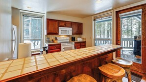 A kitchen with wooden cabinets, a microwave, a stove, and a large window. - Meadow Creek Golf Resort Condo: Skiing & Lake Life (New Meadows)