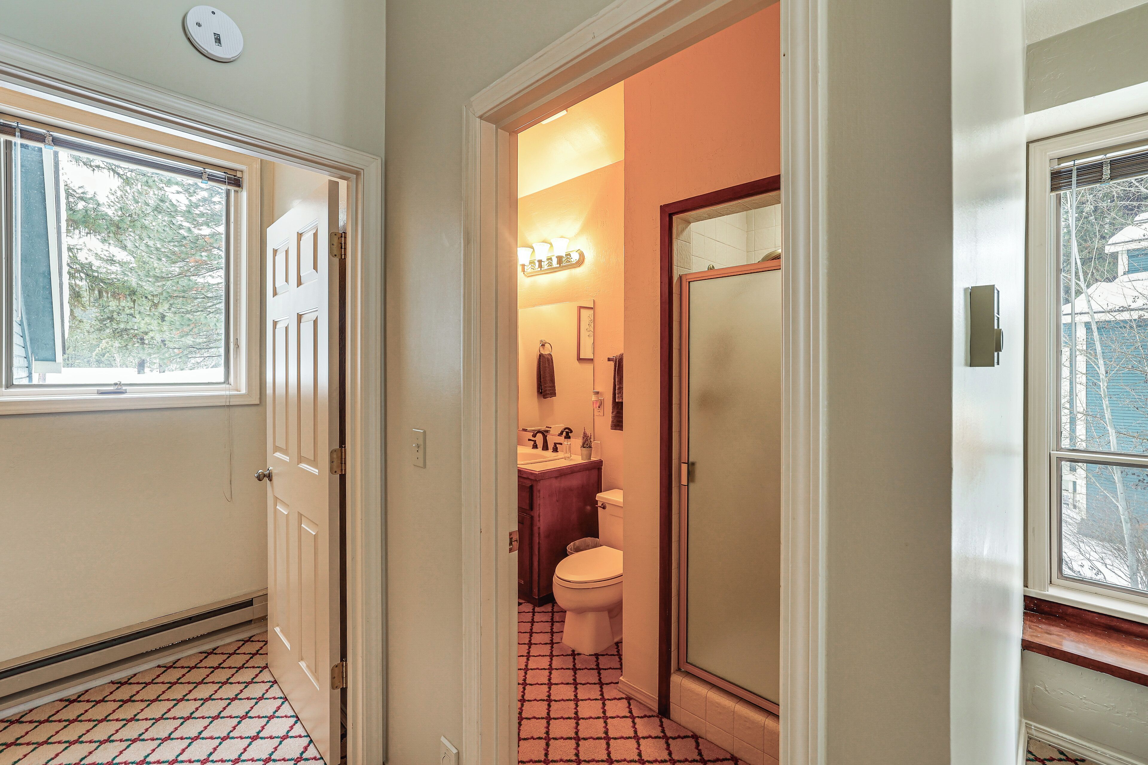Een smalle gang met een vloerkleed, die leidt naar een badkamer met toilet, wastafel en spiegel.
