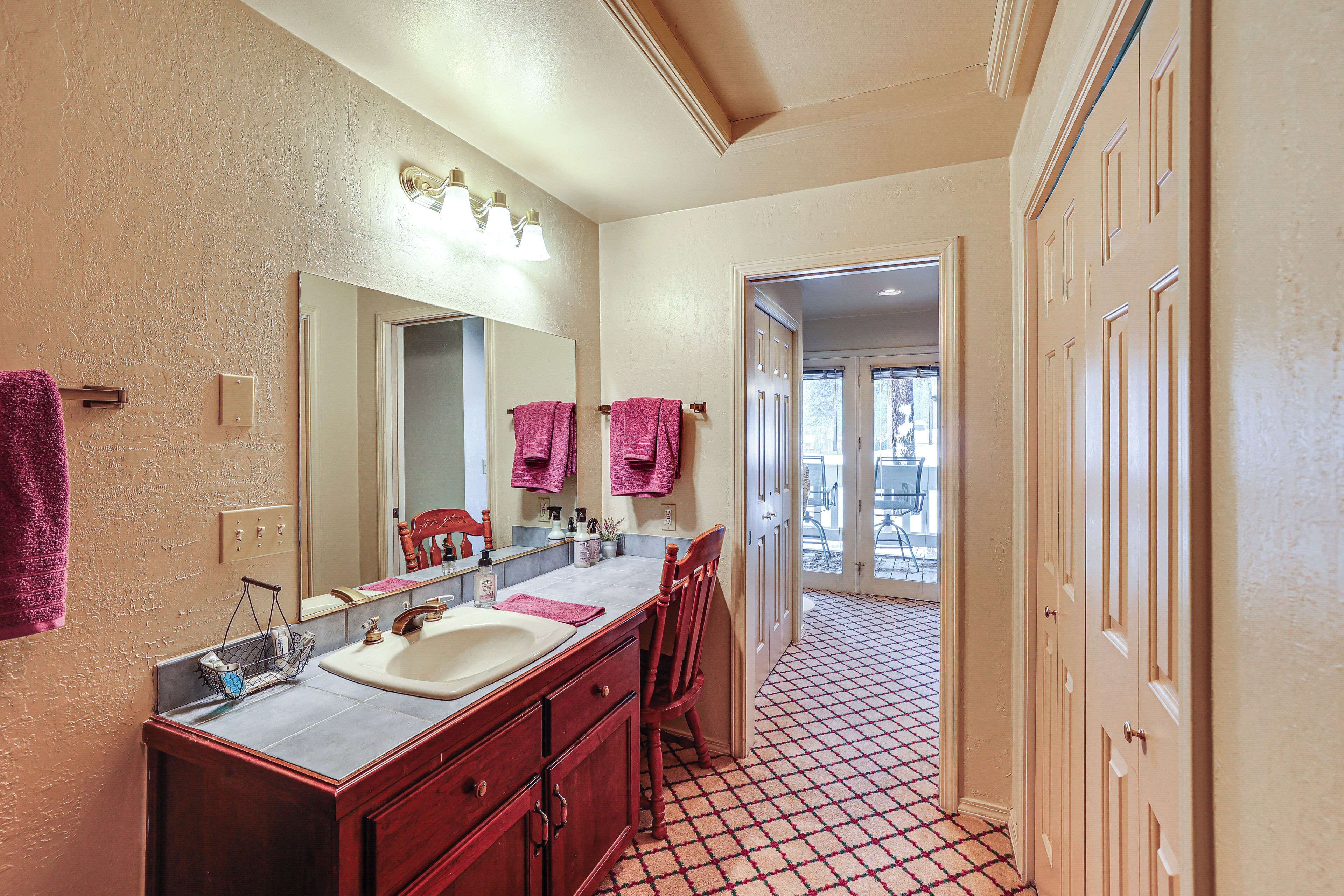 A bathroom with a large mirror, two sinks, and a chair.