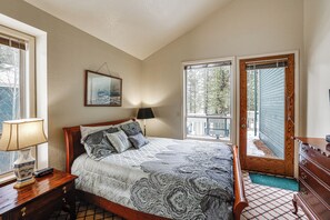 Une chambre à coucher comprenant un lit, une table de chevet, une lampe, une commode et une porte donnant sur un balcon.