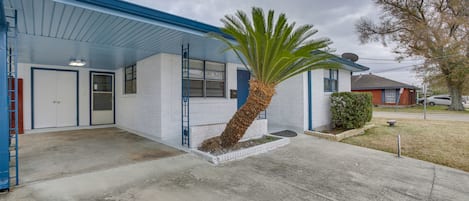 A single-story building with a blue roof and white walls, featuring a small front yard with a palm tree and a brick planter.