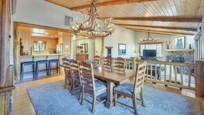 A spacious dining area with a large wooden table and chairs, a chandelier, and a view of the kitchen and living area. - Big Bear Lake Cabin w/ Hot Tub & Gas Fire Pit! (Big Bear Lake)