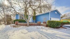 Una casa blu con un garage, immersa in un terreno innevato e alberi spogli.