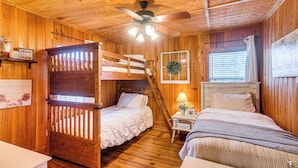 A rustic cabin-style bedroom with two bunk beds, a ceiling fan, and a small bedside table with a lamp.