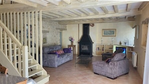 A rustic living room with a stone wall, a fireplace, two sofas, and a wooden staircase. - Agréable Maison en Pierres, à Quelques Minutes des Châteaux (vézac)