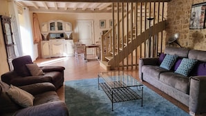 A living room with a sofa, armchairs, a glass coffee table, and a staircase leading to a kitchen. - Agréable Maison en Pierres, à Quelques Minutes des Châteaux (vézac)